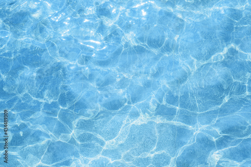 Blue, light pool water outside. Water texture on a sunny day, top view. Ripples and glare on the swimming pool surface. Natural liquid background