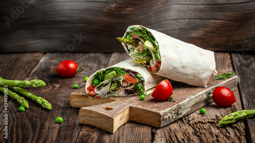 Chicken slices in a Tortilla Wrap with asparagus, avocado, tomatoes, peas, cheese and tartar sauce. fast food and junk food concept