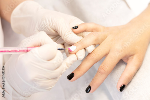Manicure in a beauty salon. A manicure master draws a French jacket with a thin brush by hand on the nails of a young girl with gel polish. Space for the text. The concept of professional care for han