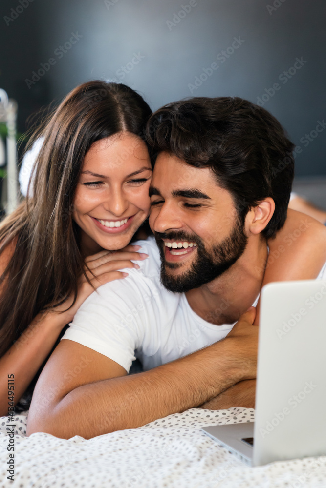 Happy young couple lying on bed at home and using laptop. Happy young couple lying on bed at home and using laptop.