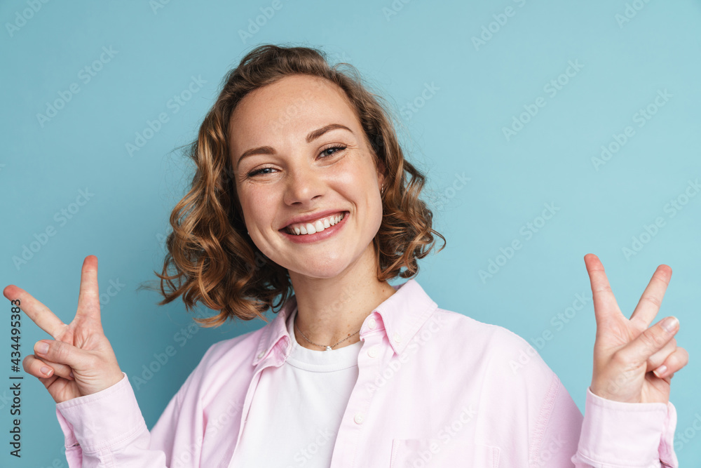 Young ginger woman with wavy hair smiling and showing peace gesture Young ginger woman with wavy hair smiling and showing peace gesture