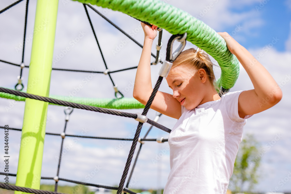 A blonde girl in a white T-shirt and sports uniform working out on the playground A blonde girl in a white T-shirt and sports uniform working out on the playground