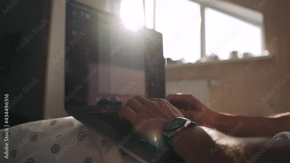 Men's hands are typing on a laptop Beautiful rays of the sun fall through the window The shadow of the sunset lies on the bed where the employee is working on the computer Slow motion Men's hands are typing on a laptop Beautiful rays of the sun fall through the window The shadow of the sunset lies on the bed where the employee is working on the computer Slow motion