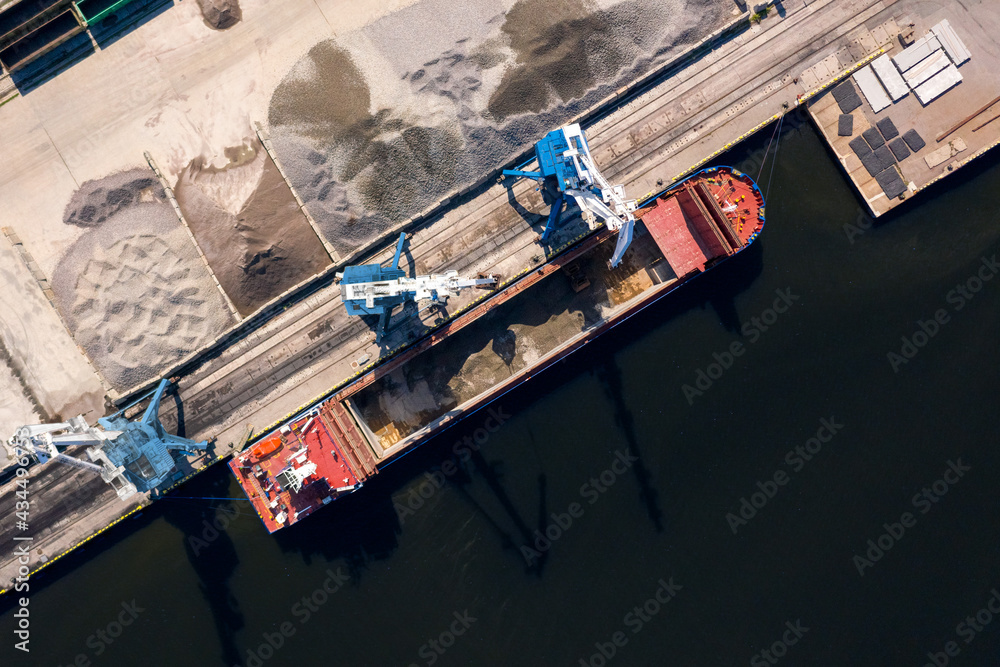 An aerial drone view of the industrial port in the Baltic Sea. There is a ships under load in the harbor.	