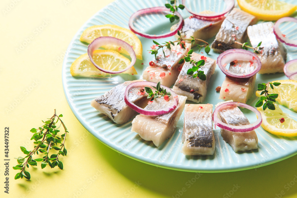 Salted herring with spice, herbs and onion on plate on yellow background with copy space. Marinated sliced fish. Food with healthy unsaturated fats, Omega 3. Top view, flat lay Salted herring with spice, herbs and onion on plate on yellow background with copy space. Marinated sliced fish. Food with healthy unsaturated fats, Omega 3. Top view, flat lay