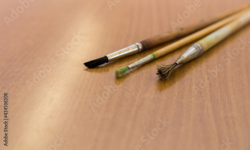Three artistic brushes lie on the table close-up. The objects for drawing with paints are put together. Wooden tassels made of squirrel and horse hair.