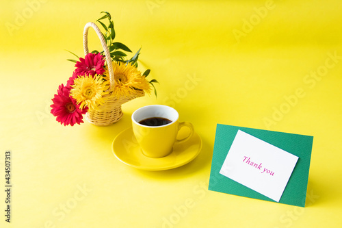 コーヒーとお礼のカードとヒマワリのような細い花びらの黄色のガーベラ（イエロースパイダー）と赤のガーベラの花かご