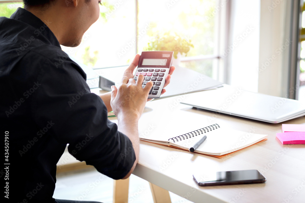 Businessman or accountant Asian young man holding calculator to calculate financial data, cost and budget Businessman or accountant Asian young man holding calculator to calculate financial data, cost and budget