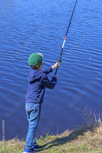 A boy is fishing on the river bank on a spring summer morning