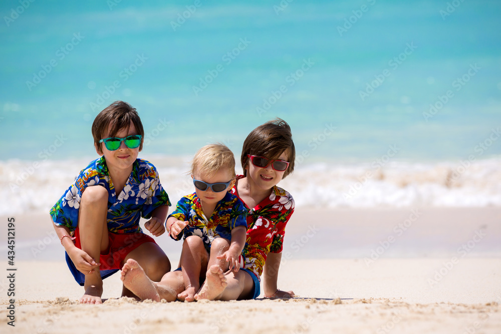 Happy beautiful fashion family, mom and children, dressed in hawaiian shirts, playing together on the beach