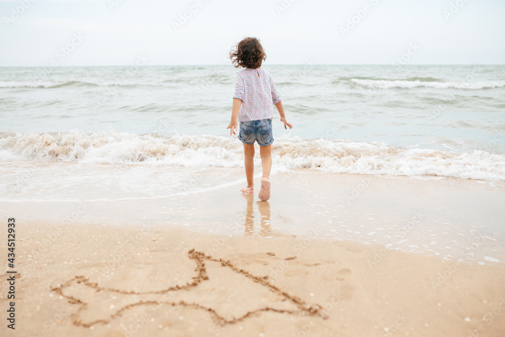Five years cute curlyFive years cute curly caucasian girl painting on sand on the beach. 