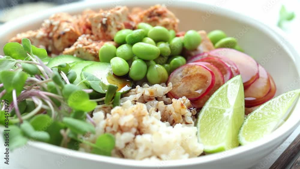 Vegan poke bowl with tofu, brown rice, beans and vegetables pouring soy sauce. Plant-based diet concept. Vegan poke bowl with tofu, brown rice, beans and vegetables pouring soy sauce. Plant-based diet concept.