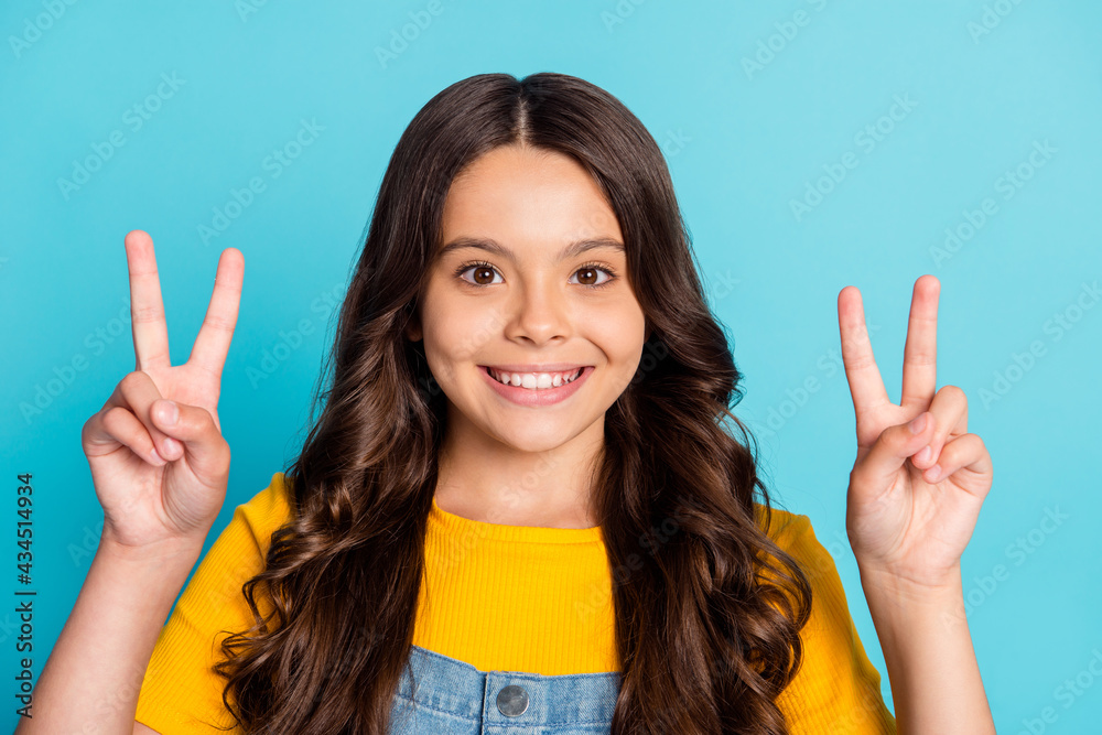 Photo of funny pretty small schoolgirl dressed yellow t-shirt showing two v-signs isolated blue color background Photo of funny pretty small schoolgirl dressed yellow t-shirt showing two v-signs isolated blue color background