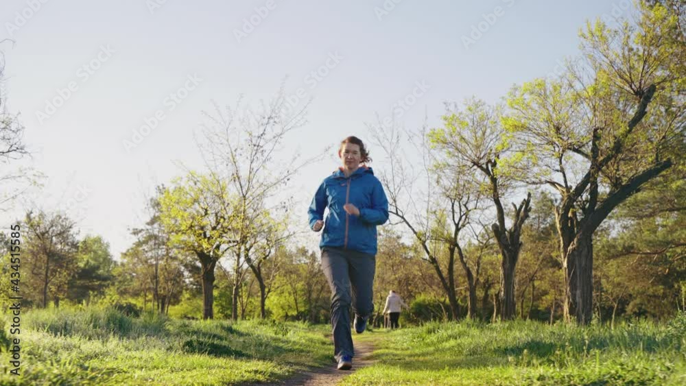 Sporty woman jogging on footpath in slow motion, dog owner and pet walking on blurred background. Tracking shot morning training in park. Concept of fitness Sporty woman jogging on footpath in slow motion, dog owner and pet walking on blurred background. Tracking shot morning training in park. Concept of fitness