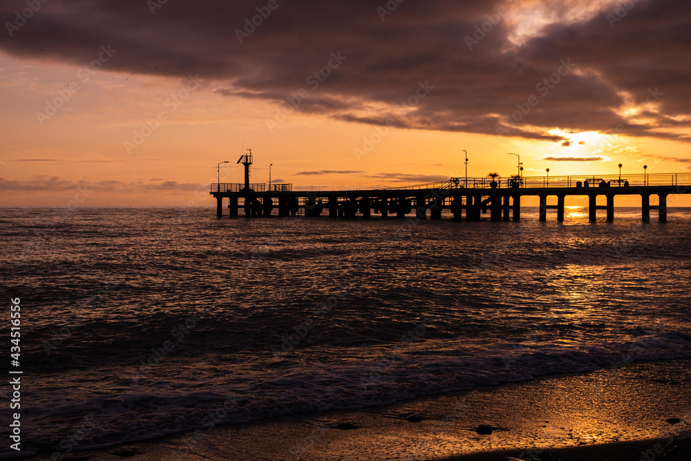 Beach with jetty at sunset on a stunning day. The sun sets over the horizon. Sunset over the sea surface.