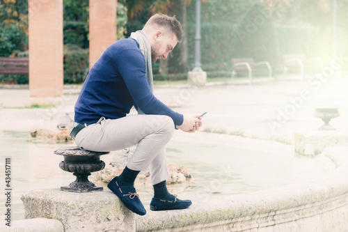 young man sitting in the fountain of a park looking at his cell phone