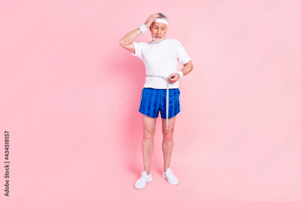 Full length body size elder man disappointed measuring himself with tape got fat need diet isolated pastel pink color background