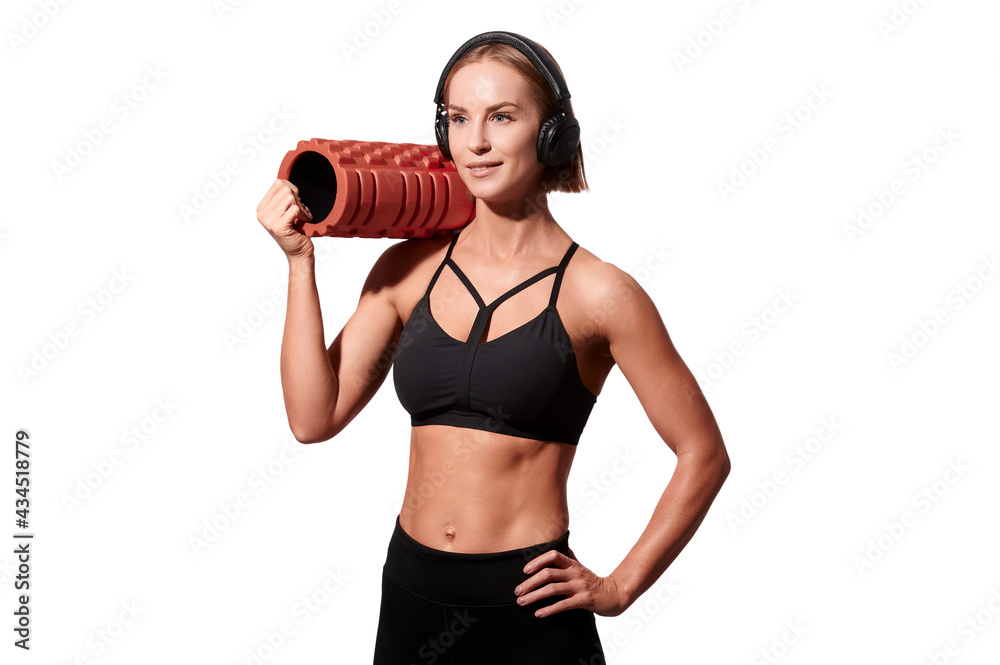 Strong athletic woman with massage roller and headphones on white isolated background Strong athletic woman with massage roller and headphones on white isolated background