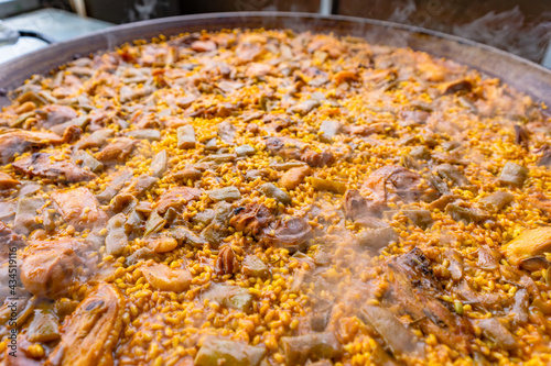 Valencian paella made of rice, chicken, rabbit and vegetables during its preparation in a big pan.