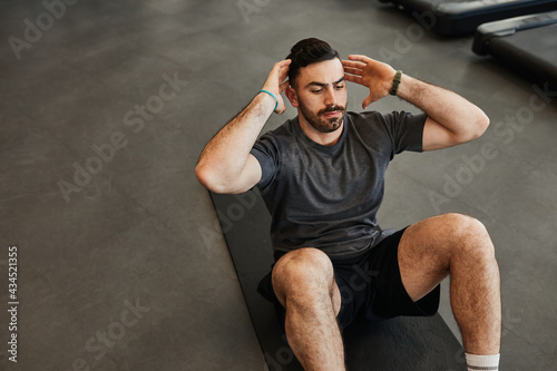 Black hair, bearded muscular man doing abs core crunch sit up exercise photo