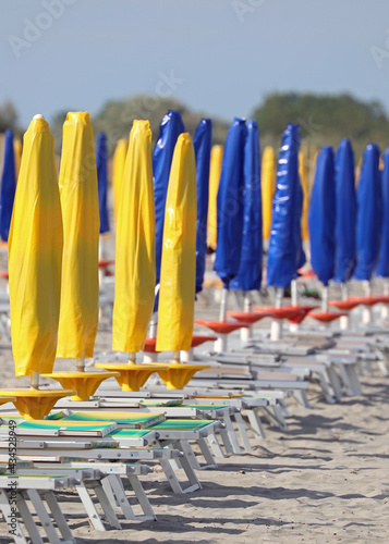 sandy beach with closed yellow and blue umbrellas with no one on the deck chairs due to the lockdown in the Resort photo