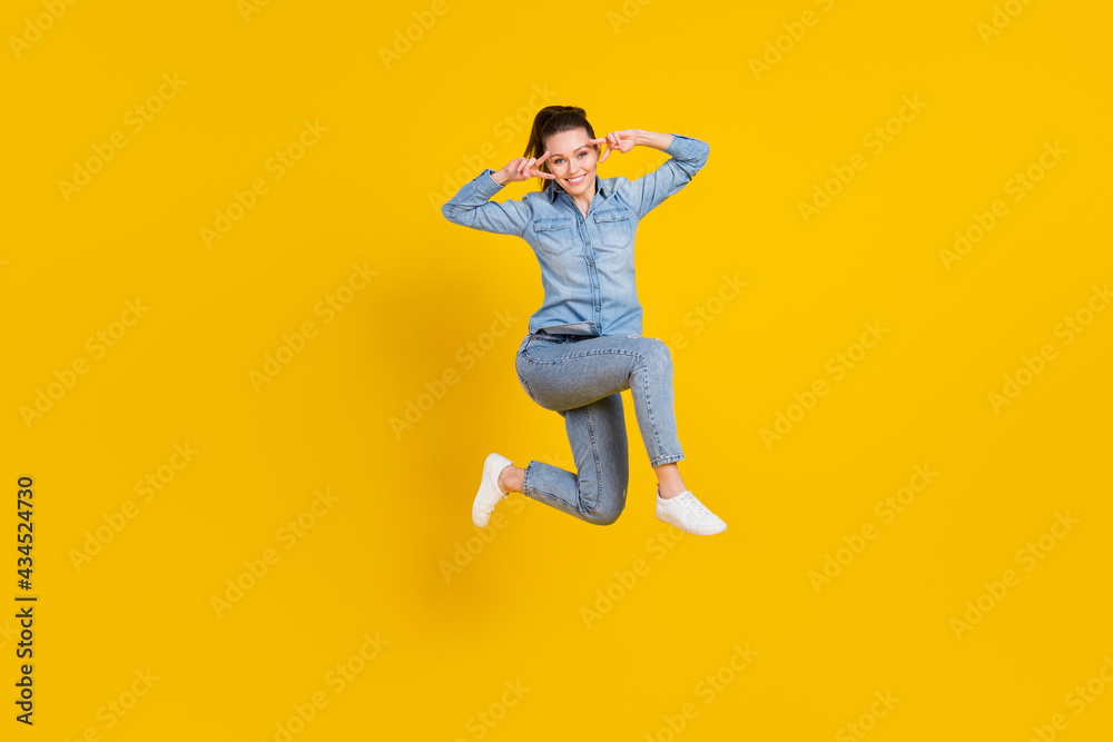 Full length body size photo young pretty girl jumping up showing v-sign gesture smiling isolated vivid yellow color background