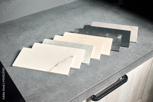 Porcelain stoneware square samples laid on kitchen countertop as examples of future kitchen fasade exterior. Porcelain stoneware exhibitor for finishing of kitchen, cabinets countertops and surfaces.