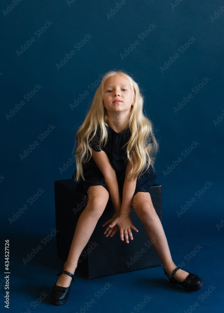 beautiful blonde in a dark blue dress on a solid blue background. The photo is great for demonstrating the character of a child - daydreaming, enthusiasm, vulnerability, touching, beauty, stubbornness beautiful blonde in a dark blue dress on a solid blue background. The photo is great for demonstrating the character of a child - daydreaming, enthusiasm, vulnerability, touching, beauty, stubbornness