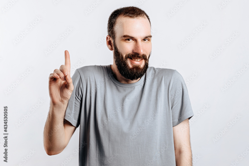 Portrait of cheerful young handsome man smiling looking at camera pointing finger upwards on white background with space for advertising mock up Portrait of cheerful young handsome man smiling looking at camera pointing finger upwards on white background with space for advertising mock up