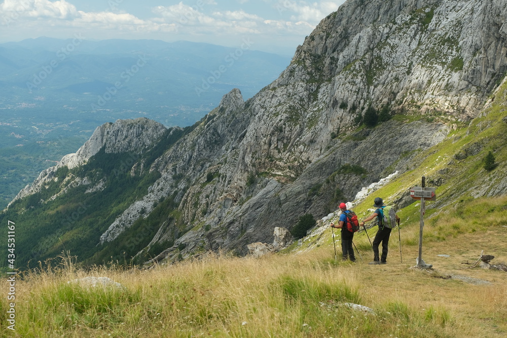 People on the trail on top of a mountain in the Apuan Alps in Tuscany.The rock at the top of the mountains contrasts with the green of the meadows and plants. 
