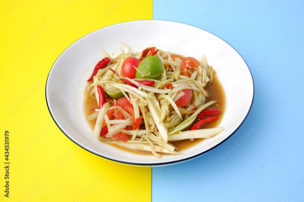 papaya salad,Raw papaya mixed lemon chili, tomato and garlic, an ingredient in papaya salad on white dish on yellow and blue background papaya salad,Raw papaya mixed lemon chili, tomato and garlic, an ingredient in papaya salad on white dish on yellow and blue background