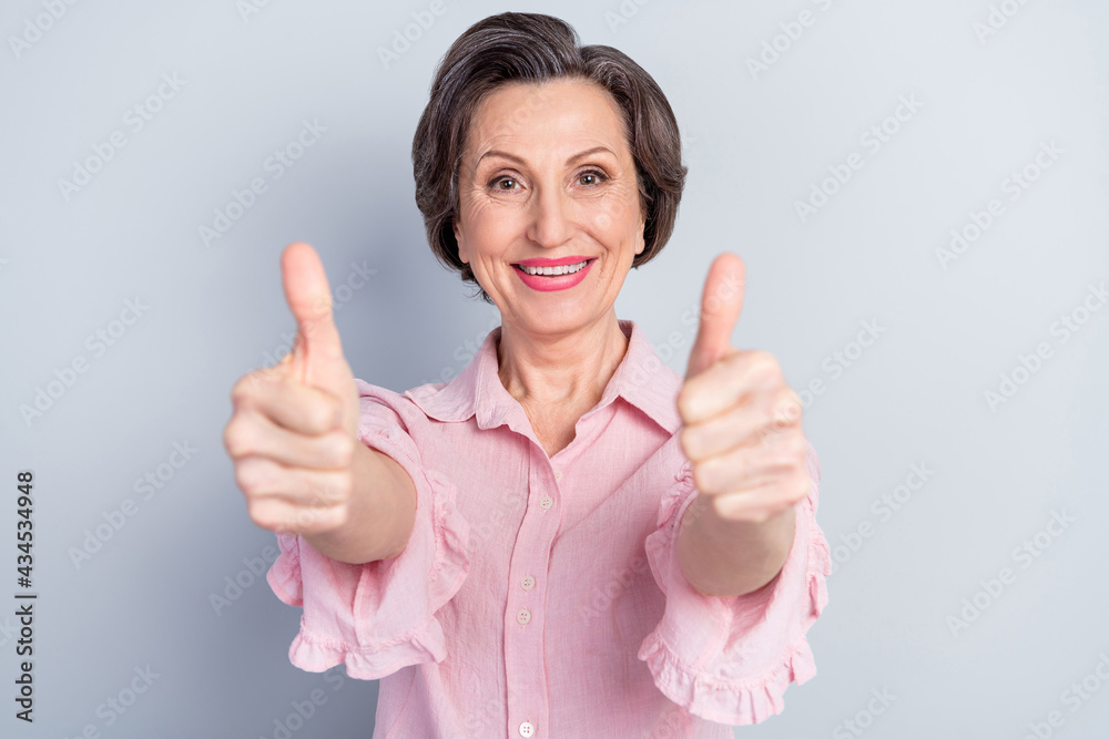 Photo of lucky cheerful age woman dressed pink shirt smiling showing two thumbs up isolated grey color background Photo of lucky cheerful age woman dressed pink shirt smiling showing two thumbs up isolated grey color background