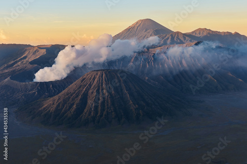 Clouds of smoke on Mount Bromo volcano, Indonesia. Aerial view of Mount as active volcano with crater in depth. Sunrise behind mountains.