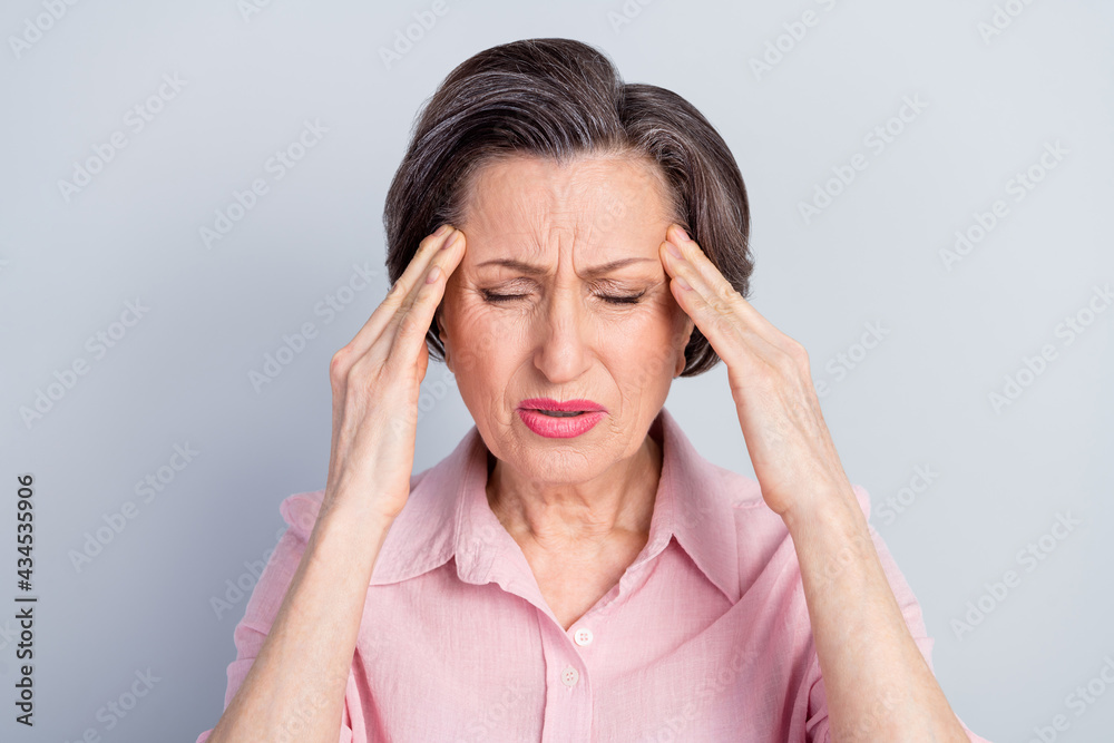 Photo of unhappy upset old woman hold hands head temples headache bad moos isolated on grey color background Photo of unhappy upset old woman hold hands head temples headache bad moos isolated on grey color background