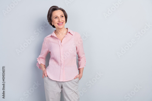 Photo of charming pretty age woman dressed pink shirt smiling arms pockets looking empty space isolated grey color background