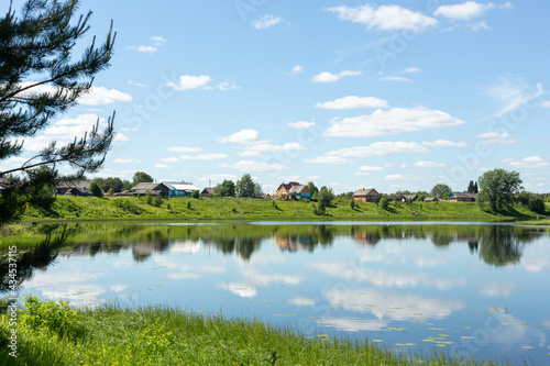 Idyllic rural landscape. Small village by the lake on a sunny summer day. The clouds are reflected in the lake