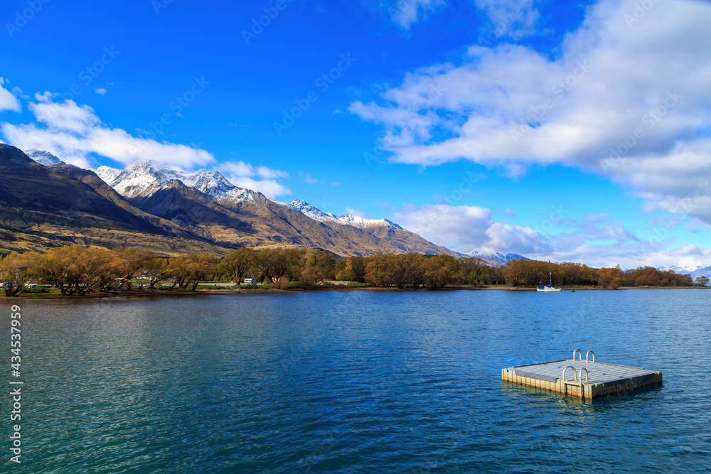Fototapeta premium Lake Wakatipu in the South Island of New Zealand, photographed at Glenorchy. The shore of the lake is ringed with autumn trees and a raft is floating in the water