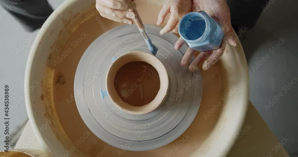 Grandmother teaches her granddaughter working on a pottery rotating wheel. Senior woman and cute little girl painting handmade pot on a spinning pottery wheel. Hobby, leisure, arts and crafts concept.