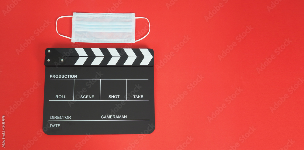 Clapper board or movie slate with face mask or medical mask isolated. it use in film,movies production and cinema industry on red background.Covid-19 or social distance concept.