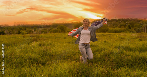 attractive woman holding an American flag in the wind in a field. Summer landscape against the blue sky. Horizontal orientation.