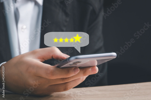 Customer service evaluation and satisfaction survey concepts. Customer hand hold smartphone and touching on screen with gold five star rating excellent feedback icon, Rated a very good review.