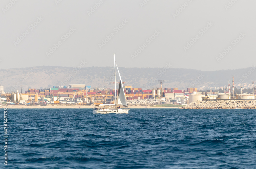 A private yacht sails in the waters of the Haifa Bay, against the background of Haifa port, in the Mediterranean Sea, near the port of Haifa in Israel