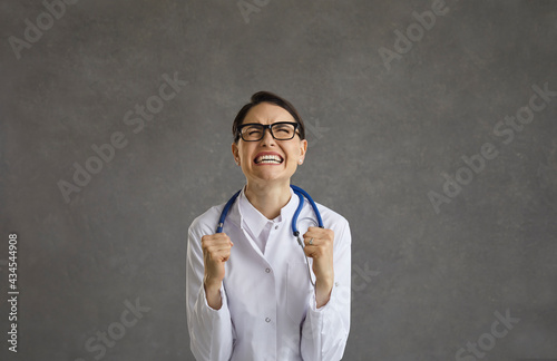 Excited young female doctor standing with yes closed and clenched fists showing gesture winner. Studio shot face portrait. Victory, success and achievement in health healthcare medicine concept
