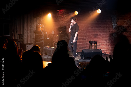 Fototapeta Young Caucasian male comedian performing his stand-up monologue on a stage of a