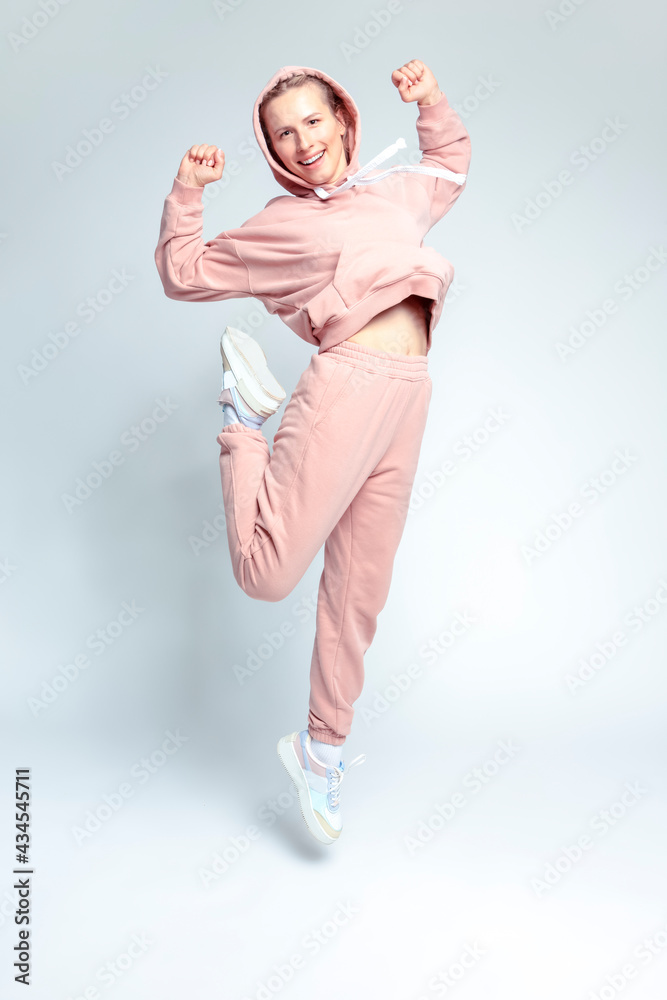 Active and Positive Laughing Caucasian Female In Hood Streetwear During Dancing and Stretching Exercises On White Background.