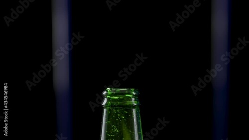 Macro shot of cap popping out of green glass bottle and explosion of splash carbonated beer. Amber liquid under pressure bursts out of bottle and fountains up. Black background. Close up. Slow motion. photo