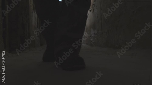 The feet of a man walking down the dark corridor of an old abandoned basement. Front view. Low key