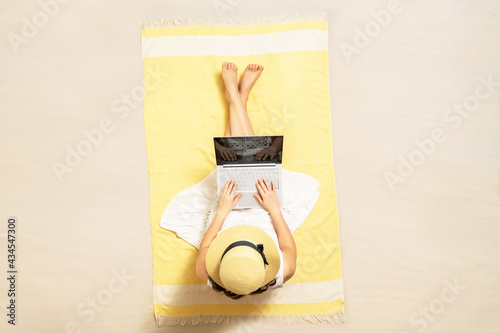 Woman with laptop sitting on the beach towel and enjoying summer vacation. Top view