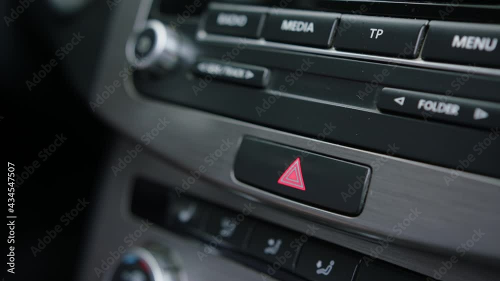 Close-up of male caucasian hand pressing emergency light button on car dashboard. Activating the hazard lights of a vehicle by pressing the button on the dash Close-up of male caucasian hand pressing emergency light button on car dashboard. Activating the hazard lights of a vehicle by pressing the button on the dash