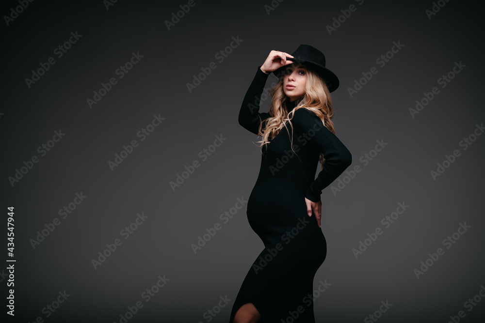 Beautiful pregnant woman in black dress and hat on dark background Beautiful pregnant woman in black dress and hat on dark background